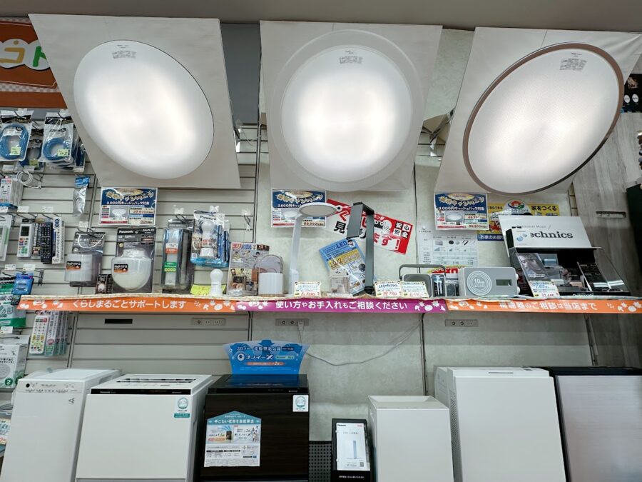 LED照明器具のシーリングが3種類壁に斜めに展示されている。その下には懐中電灯や玄関照明なども置いている。その下には加湿空気清浄機やジアイーノという空間除菌脱臭機を展示。