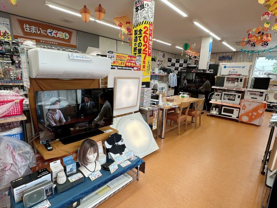 電ねっとクリハラの入り口正面の写真。天井は秋の装飾のドングリや紅葉が飾ってあります。正面に入ってエアコンや有機ELテレビ、小物商品が展示されています、2027年までに蛍光灯の製造と輸出入が廃止されるにあたりLED照明もシーリングと和室シーリングを展示。